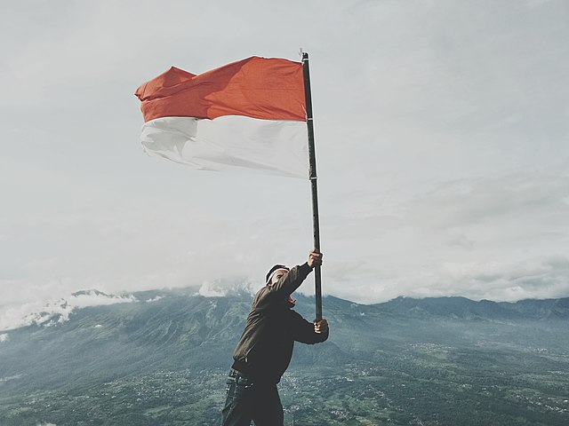 Seorang pemuda sedang mengibarkan bendera Indonesia di puncak gunung penanggungan, jawa timur, Indonesia dengan latar pegunungan.